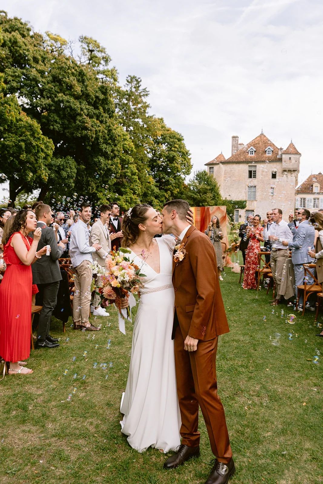 Les mariés s’embrassent au milieu de l’allée, entourés des invités debout dans le jardin.