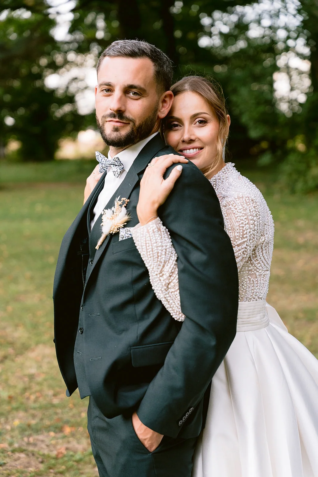 La mariée enlace le marié par-derrière et sourit par-dessus son épaule.