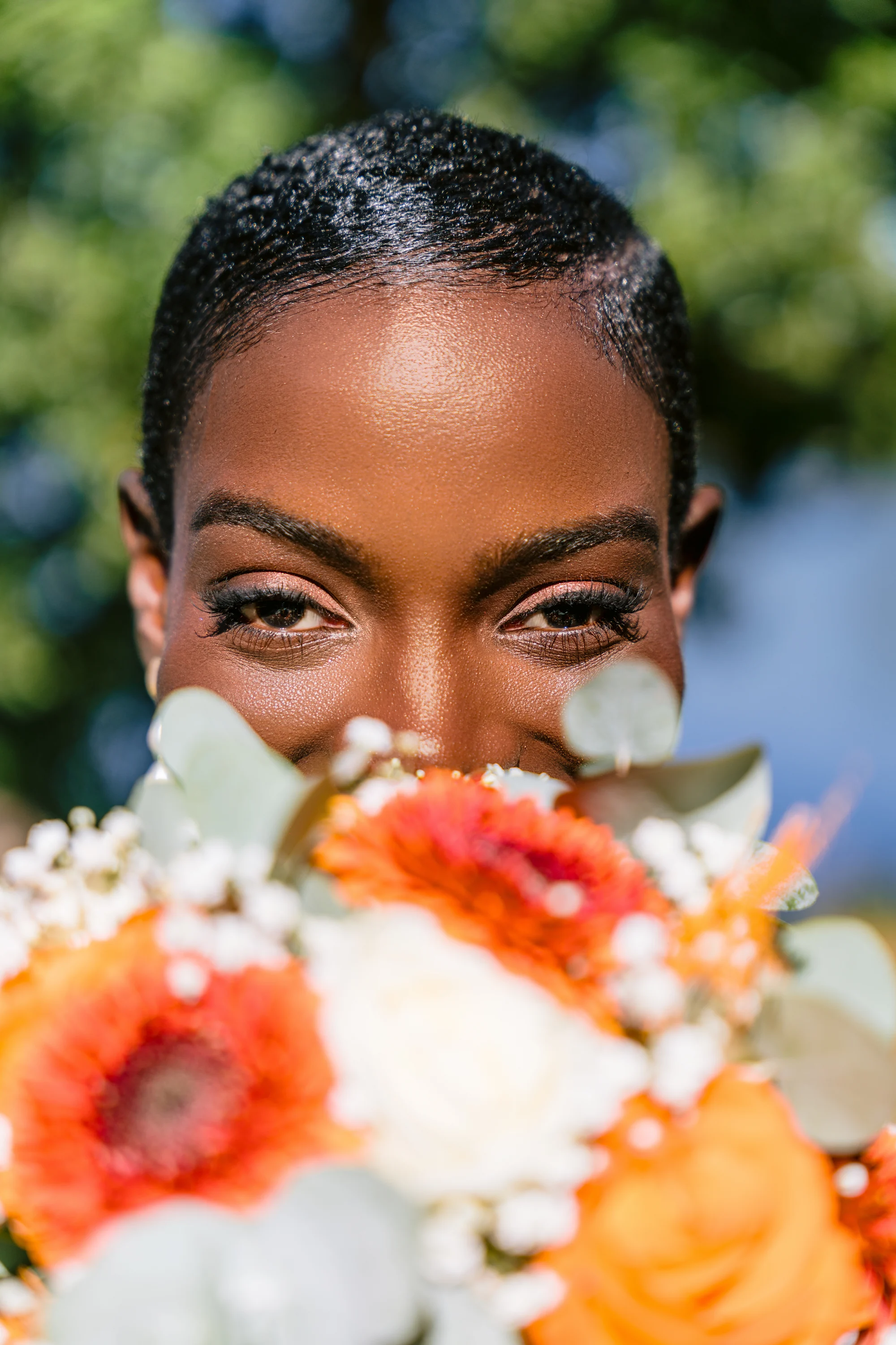 La mariée regarde par-dessus son bouquet de fleurs orange et blanches.
