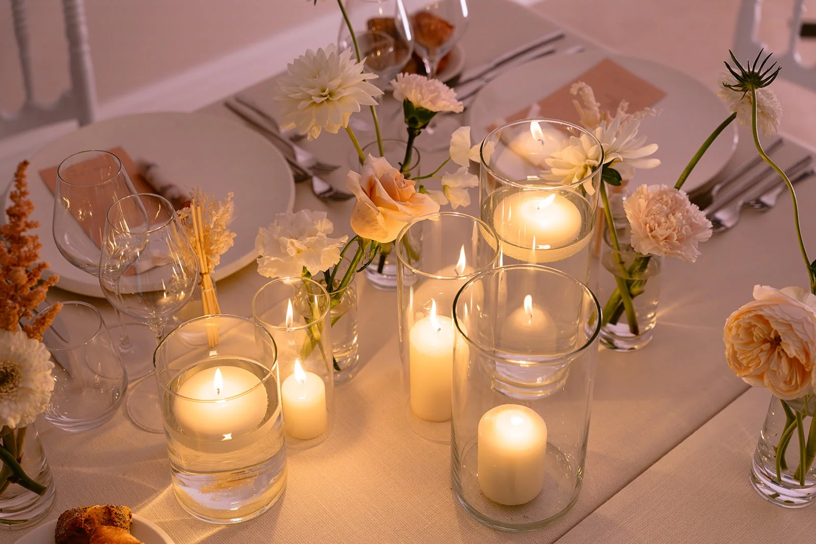 Des bougies allumées et des fleurs pastel éclairent la table de réception.
