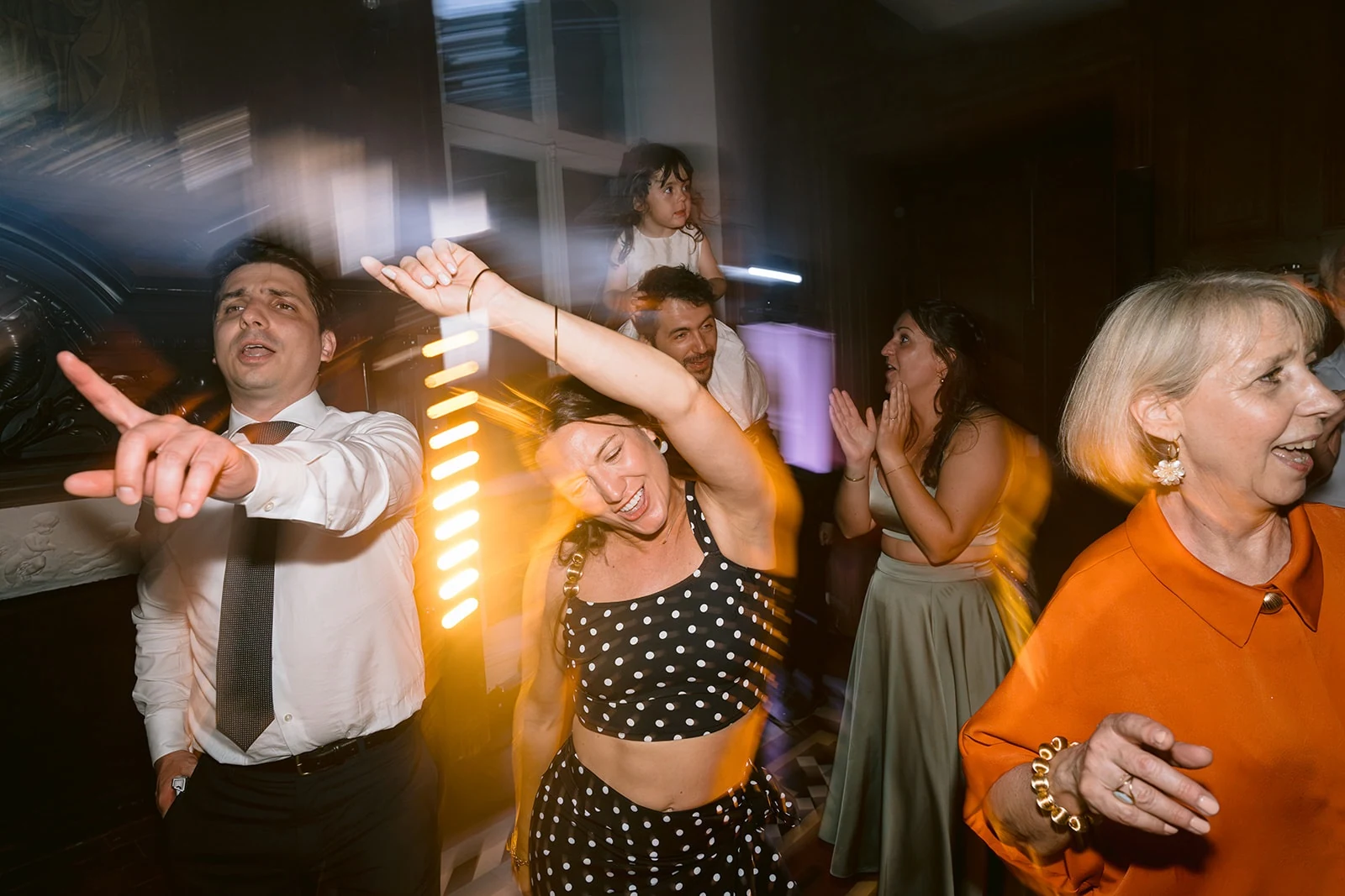 Des invités dansent en levant les bras sous les lumières de la soirée, avec un flou de mouvement.