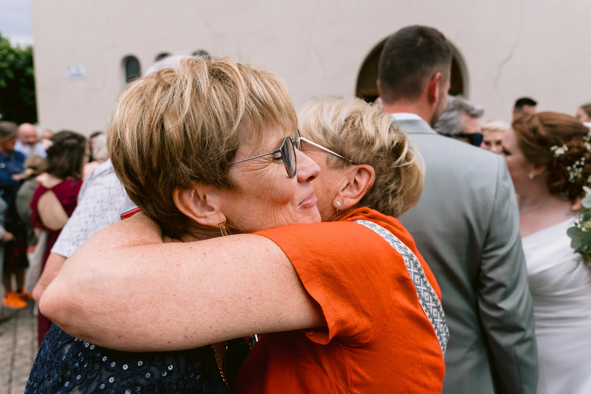 Deux invitées se serrent dans les bras et s’embrassent à la sortie de la cérémonie.