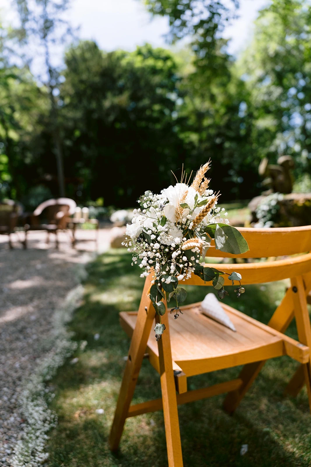 Un petit bouquet blanc et du feuillage décorent une chaise en bois de la cérémonie en plein air.